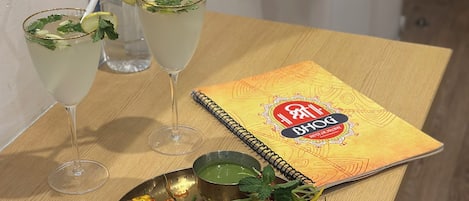 Una mesa con un plato de comida, dos bebidas, una botella y un libro.