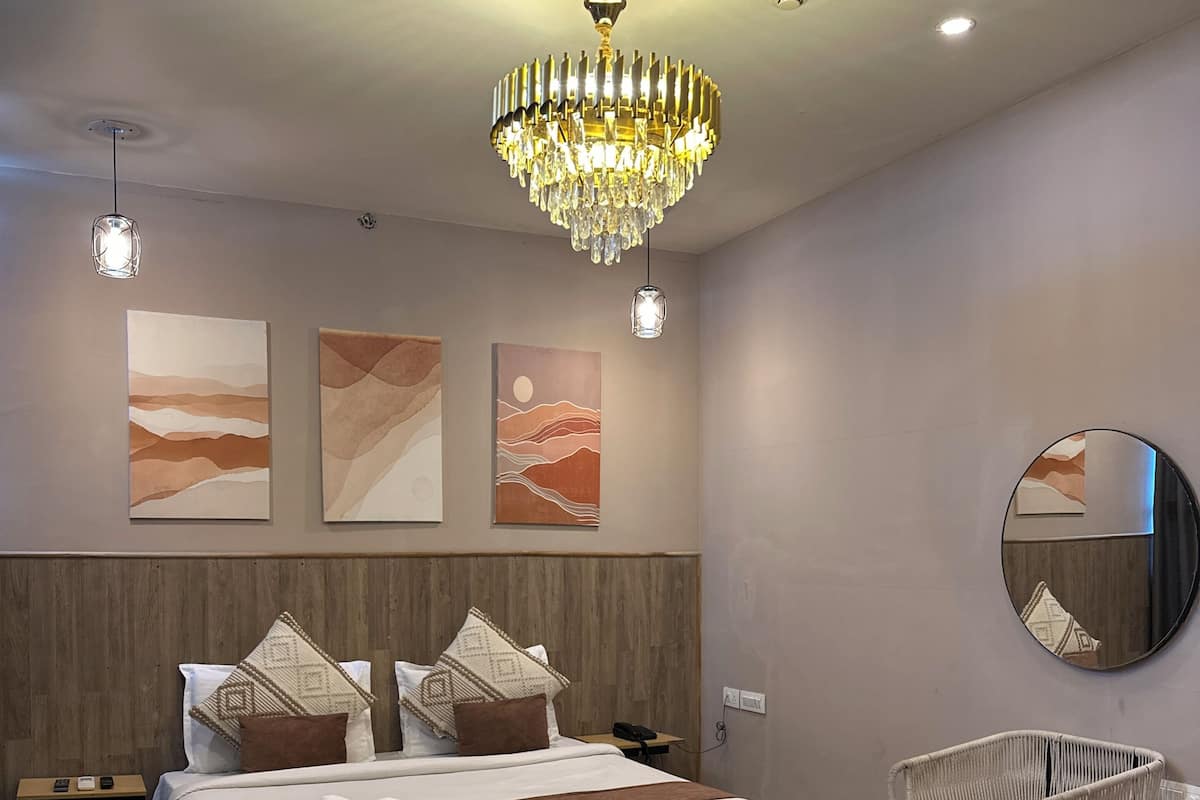 A modern bedroom with a large bed, a chandelier, artwork on the wall, a round mirror, and a wicker chair.