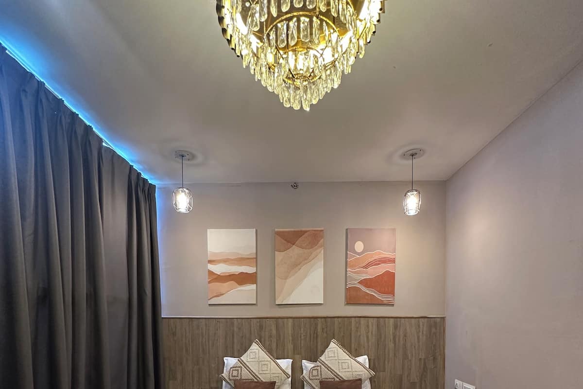 A modern hotel room with a large bed, a chandelier, artwork on the wall, and a desk with a phone.