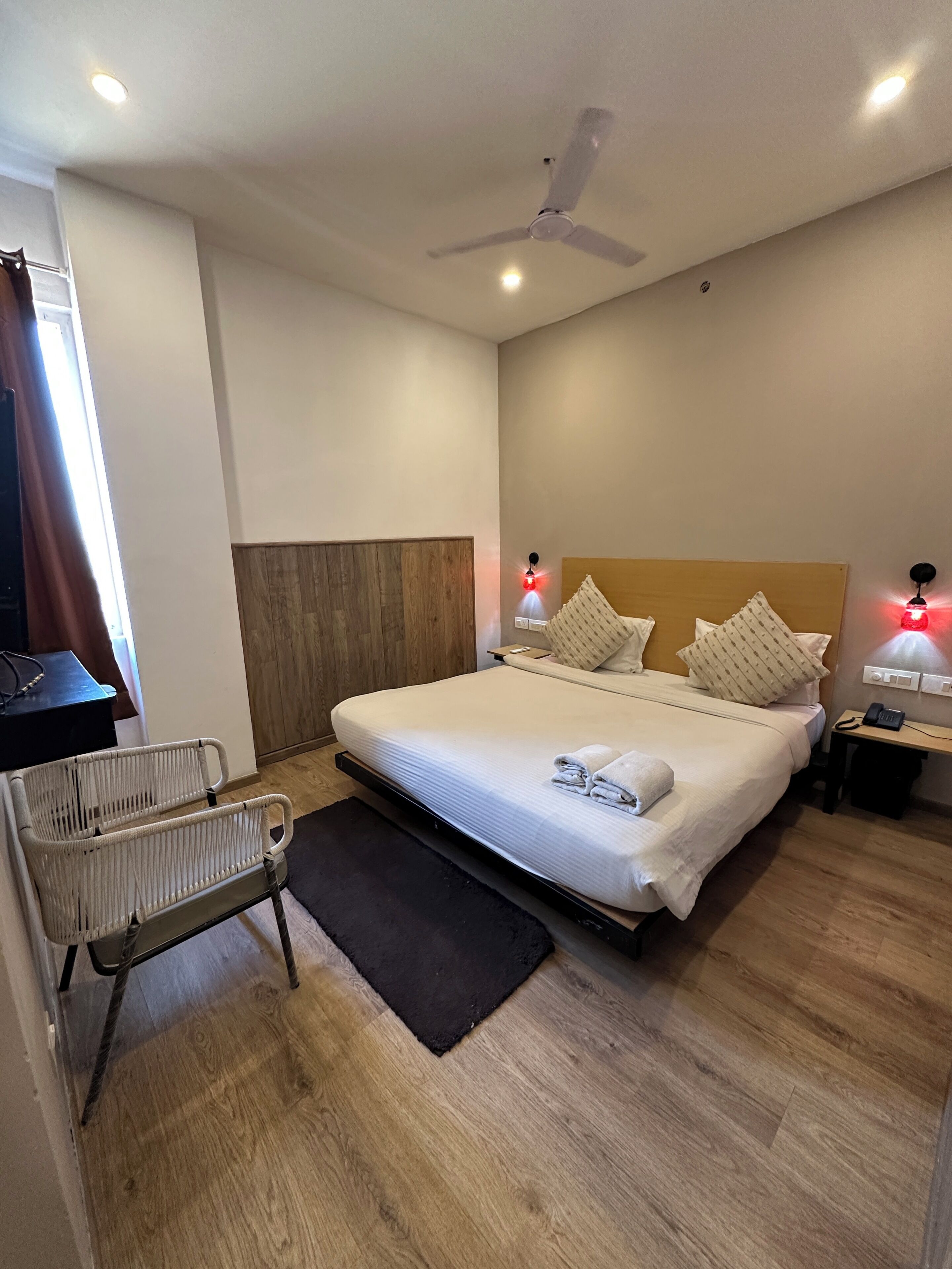Une chambre d’hôtel moderne équipée d’un lit, de lampes de chevet, d’un ventilateur de plafond et d’une petite table avec un téléphone.