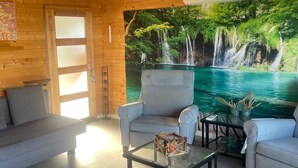 Une pièce au décor intérieur en bois, avec un canapé, un fauteuil, une table en verre et un grand tableau représentant une cascade.