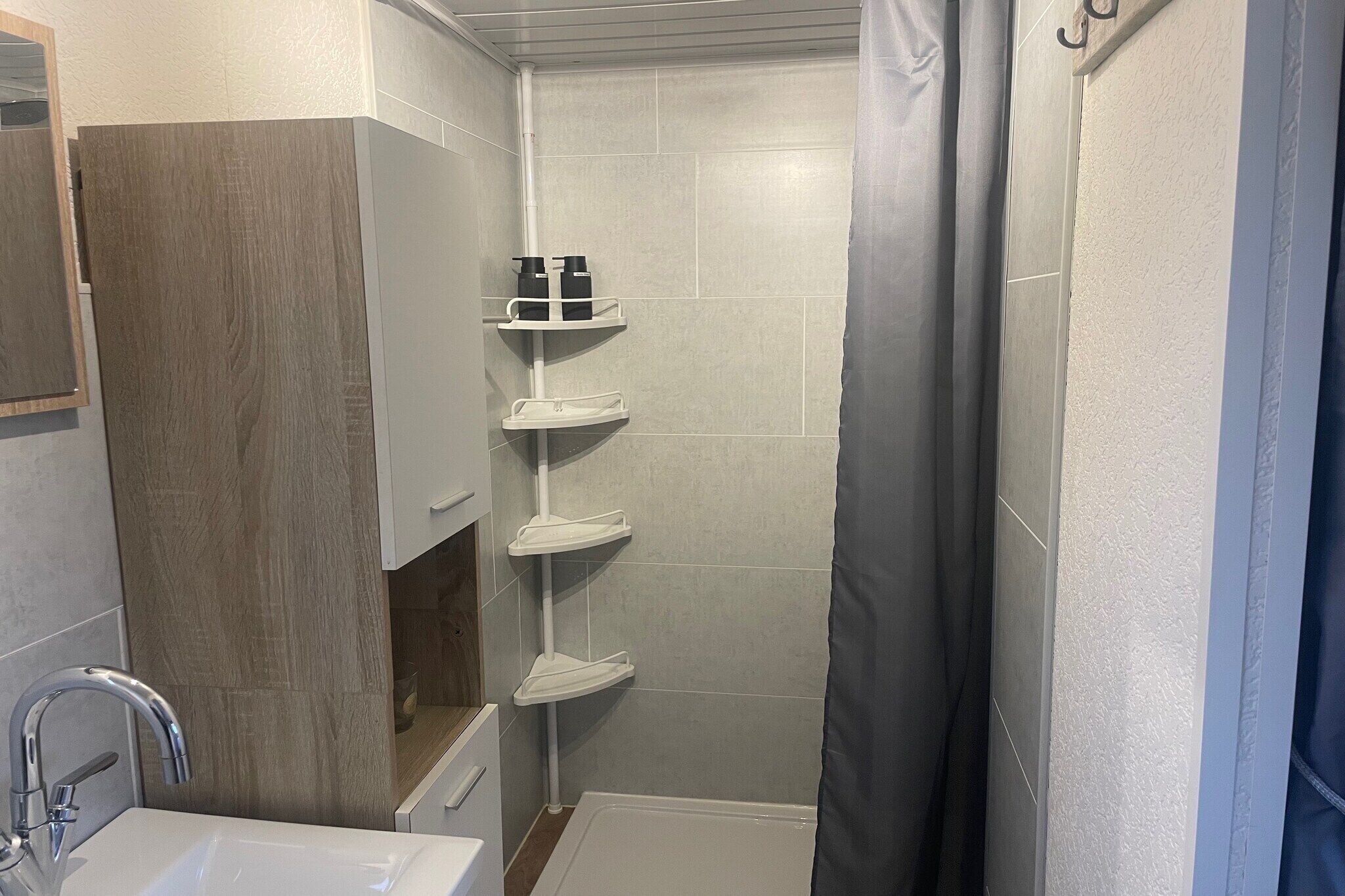 Un baño con ducha, lavabo e inodoro. Hay estantes con artículos de aseo.