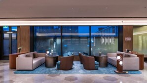 Eine moderne Lobby mit einer Sofagarnitur, runden Tischen und einem großen Fenster mit Blick auf die Stadt.