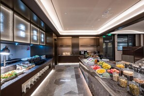 A modern hotel kitchen with a buffet area featuring various food items and a coffee station.