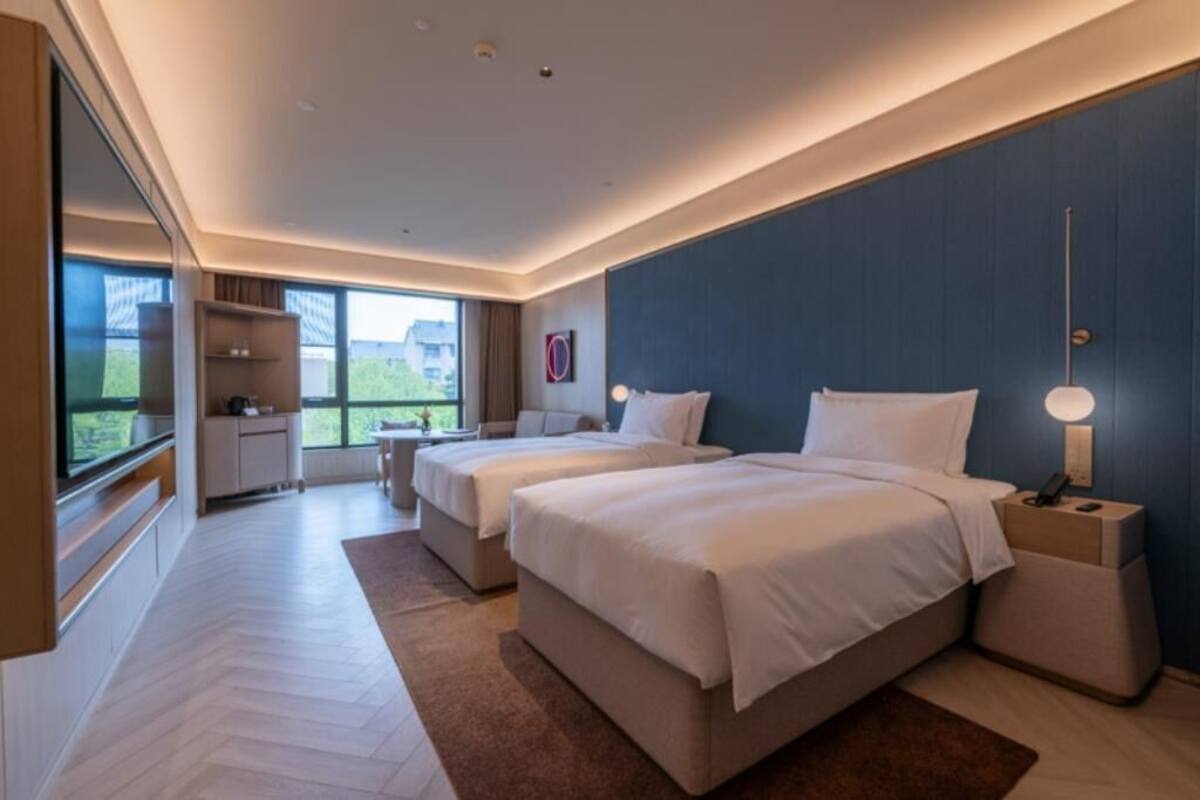 Moderni hotellihuone, jossa on kaksi sänkyä, työpöytä, tuoli, televisio ja suuri ikkuna.