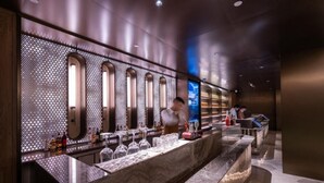 Eine Bar mit einer Marmorplatte, mehreren Gläsern, Flaschen und einer Wand mit Bogenfenstern und Muster.