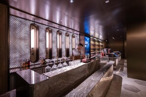 Eine Bar mit einer Marmorplatte, mehreren Gläsern, Flaschen und einer Wand mit Bogenfenstern und Muster.