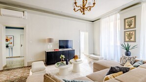 Een woonkamer met een zithoek, een televisie, een kroonluchter en een vloer met een patroon.