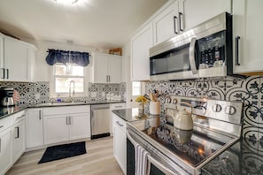 Una cocina moderna con armarios blancos, un microondas de acero inoxidable y un horno.