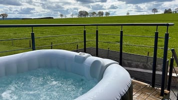 En oppustelig jacuzzi på en terrasse med udsigt over en græsplæne og træer.