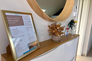 Ein gerahmtes Hinweisschild auf einer Holztischplatte, darüber ein Spiegel, eine dekorative Vase mit goldenen Blättern und ein kleiner Blumentopf.