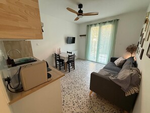 Ein kompakter Wohnbereich mit Küchenzeile, Essplatz, Sofa und Deckenventilator.