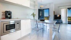 Een moderne keuken met een inbouwmagnetron, een koffieapparaat en een eethoek met transparante stoelen en een tafel.