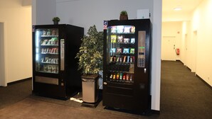 Two vending machines in a hallway with a potted plant between them. - nurHotel (Reinbek)