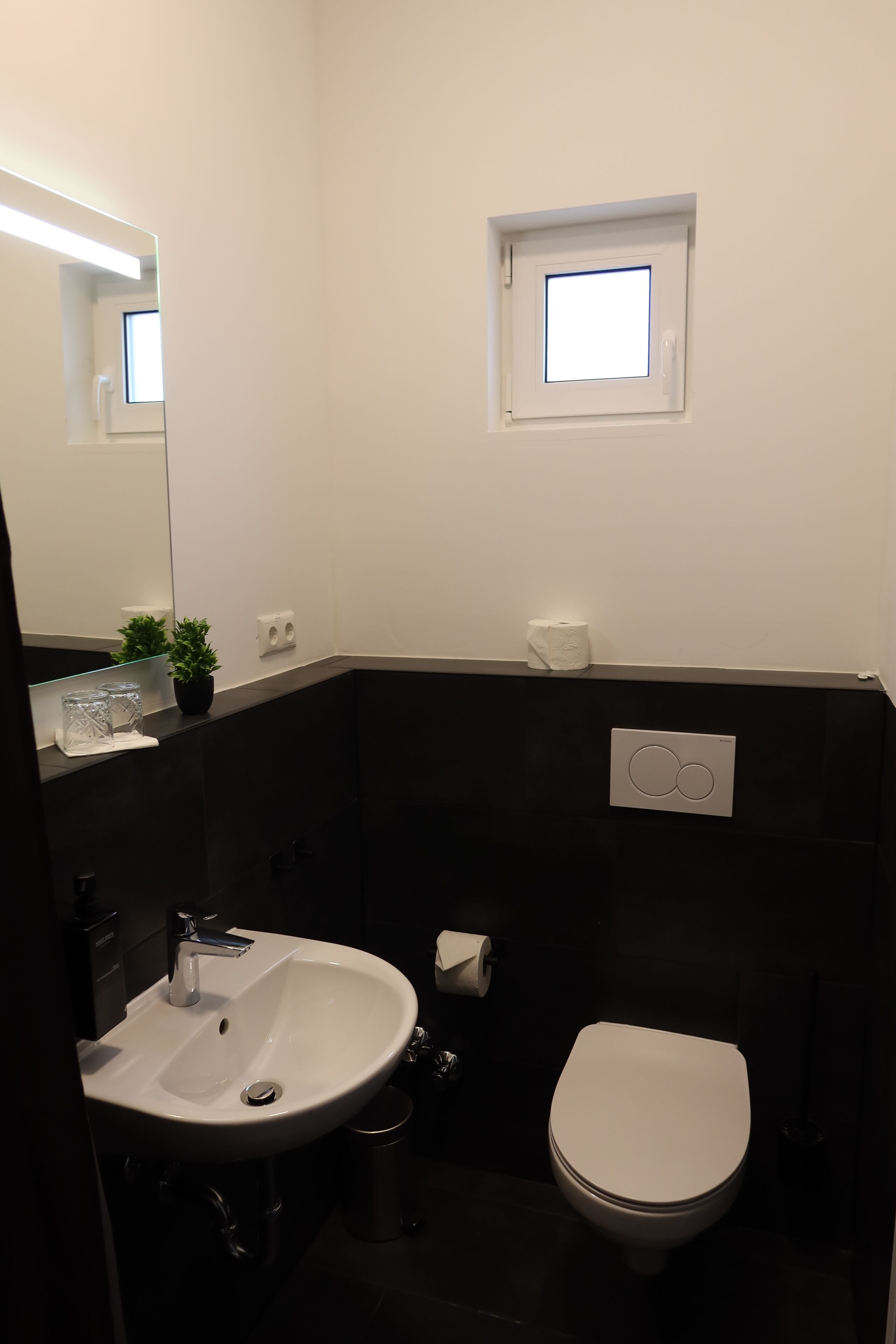 A bathroom with a white sink, a toilet, a small window, and a mirror.