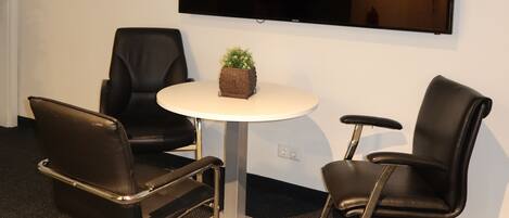 Una sala de conferencias con una mesa redonda, dos sillas, un televisor de pantalla plana y una planta pequeña.