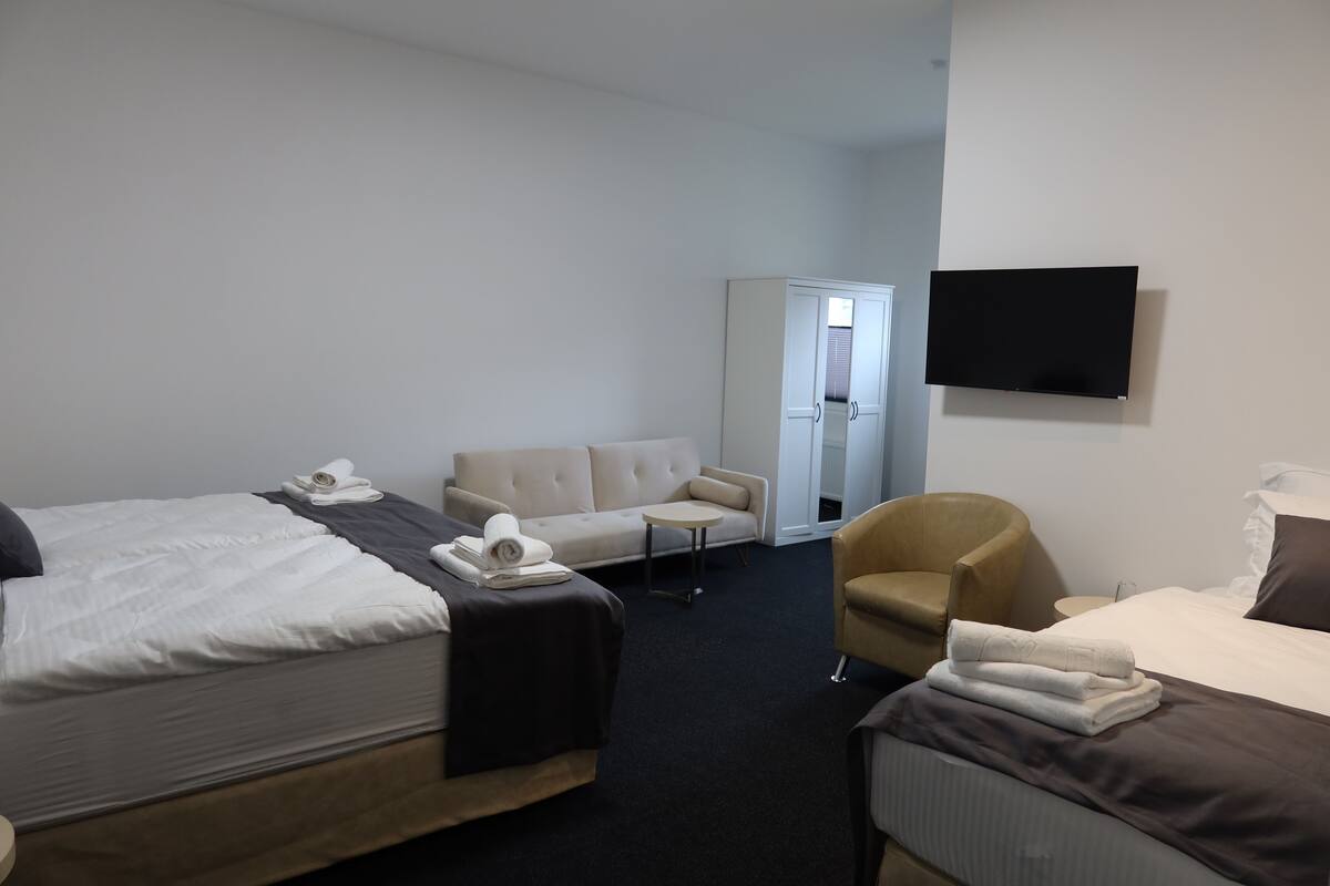 A hotel room with two beds, a sofa, a chair, a TV, and a door leading to a bathroom.