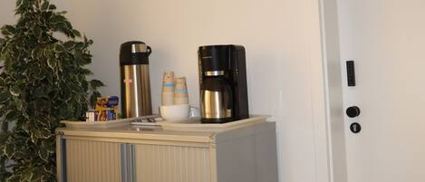 A kitchenette with a coffee maker, a kettle, and a plant.