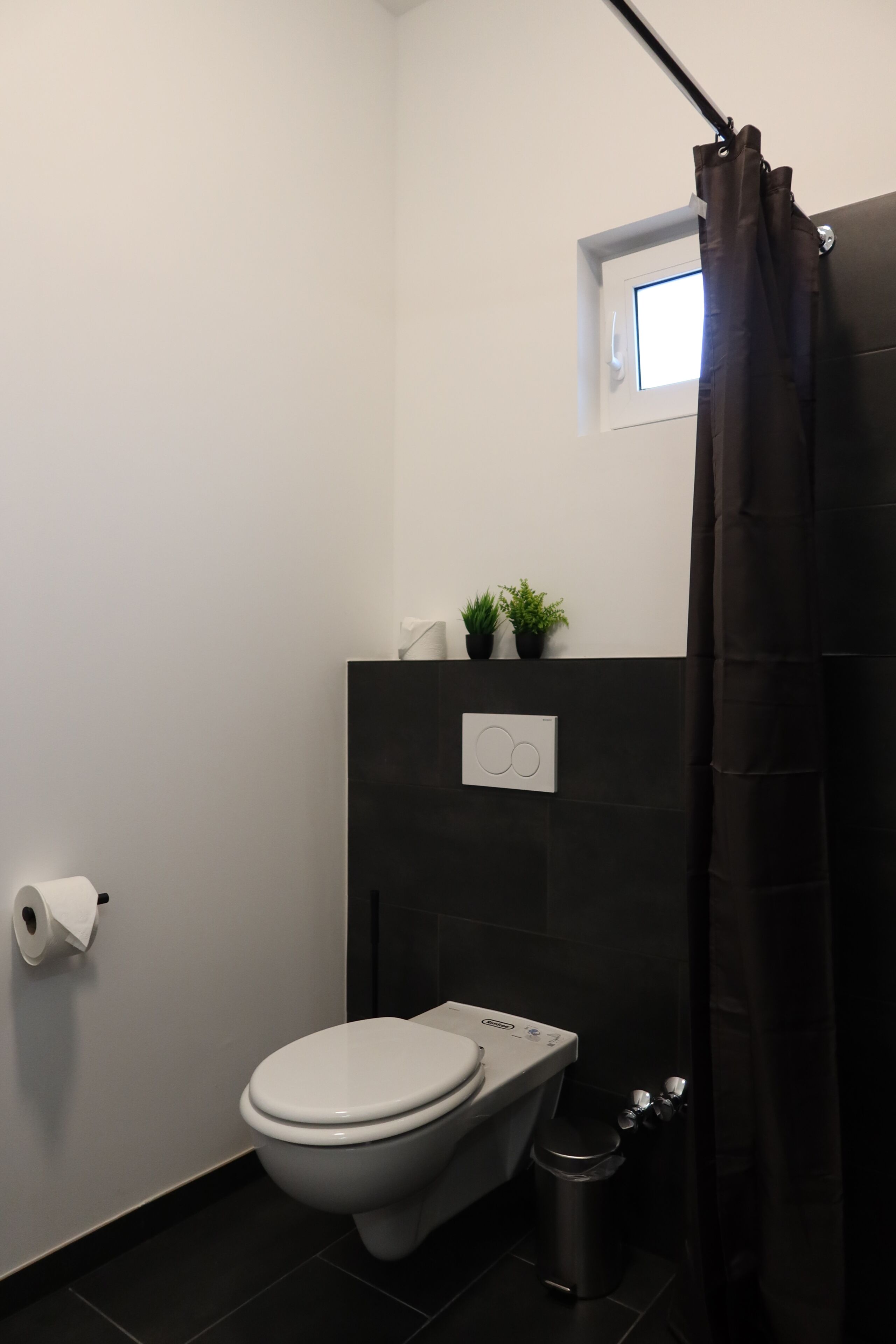 Une salle de bain moderne équipée de toilettes, d’une poubelle, d’une petite fenêtre et d’un rideau de douche.