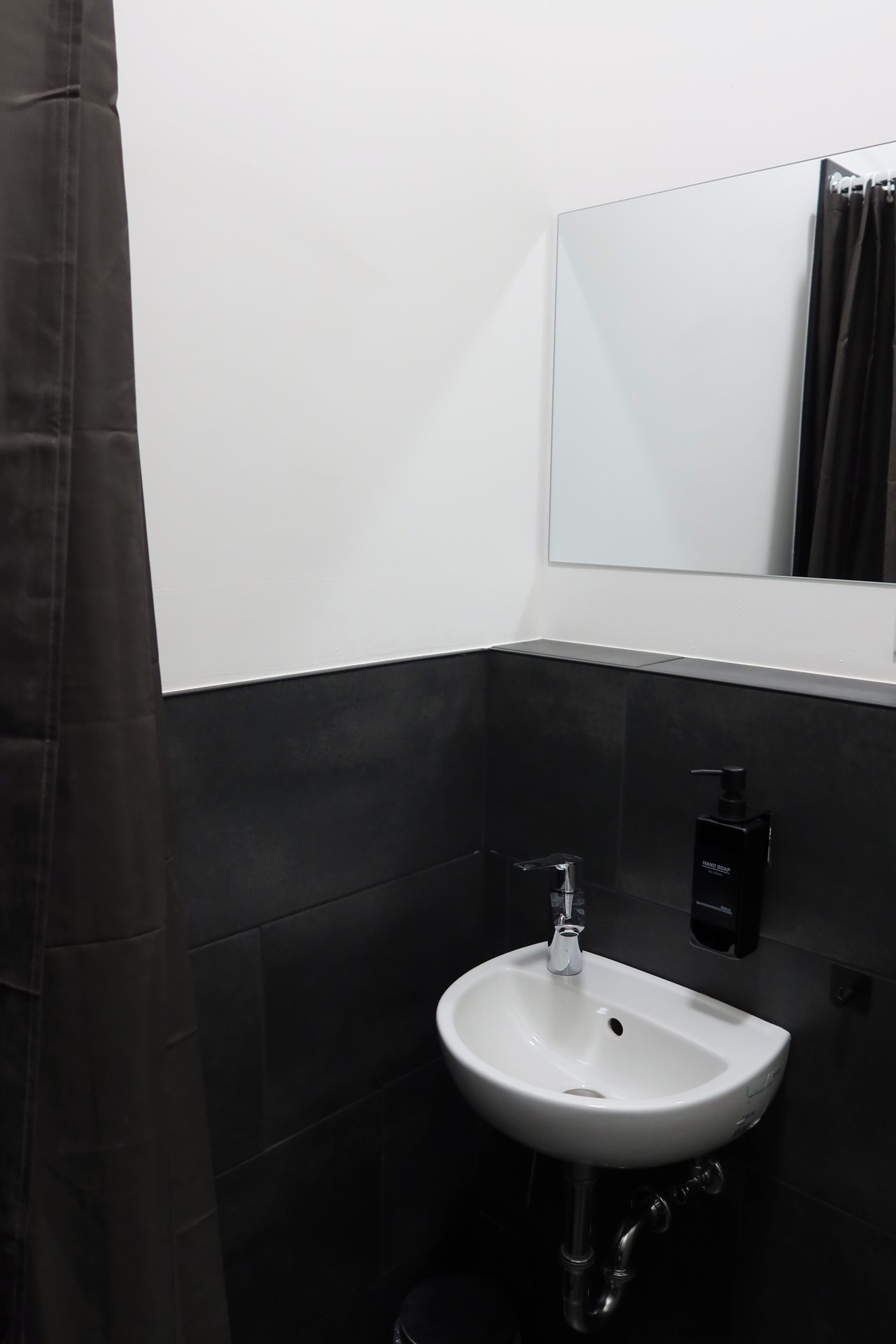 Un baño con un lavamanos blanco, un espejo y un toallero negro.