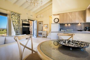 A modern kitchen with wooden cabinets, a dining area with a glass table, and a living room with a sofa and chairs. - Orion Luxury Villa, Estrellas Luxury Villas (Kefalonia)