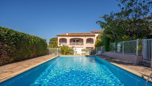 Una piscina con superficie d'acqua cristallina e blu, circondata da una recinzione bianca, e un edificio con tetto in tegole sullo sfondo.