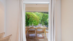 Zona pranzo con tavolo apparecchiato per quattro, una sedia e vista su un giardino tramite una porta di vetro.