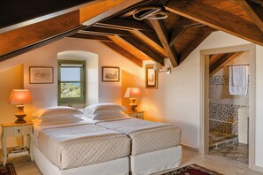 Ein Schlafzimmer mit Schlafgalerie, einem Bett mit weißer Bettwäsche, zwei Nachttischlampen und Blick auf eine geflieste Treppe.