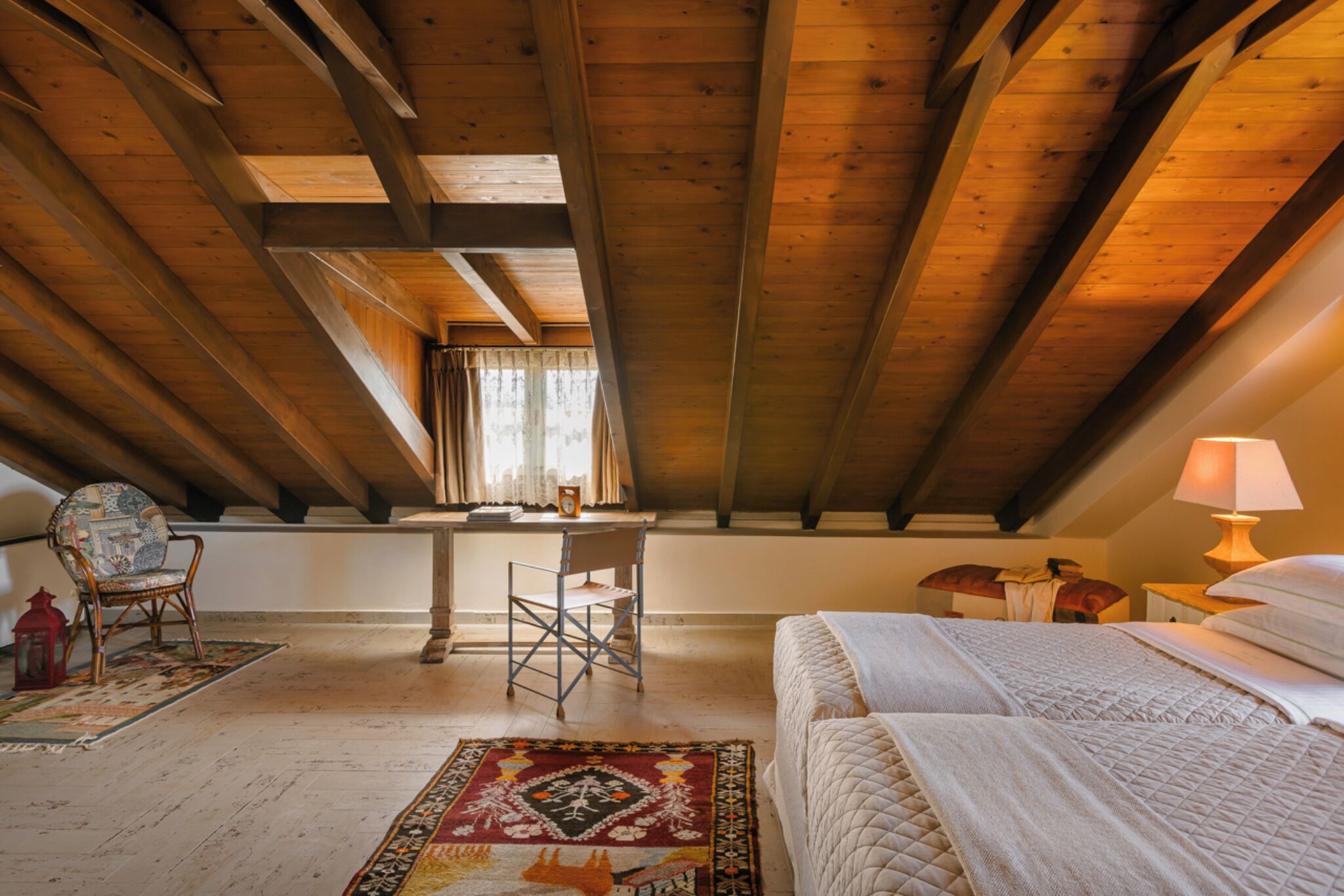 A room with a sloped ceiling, a bed, a desk, and a chair.