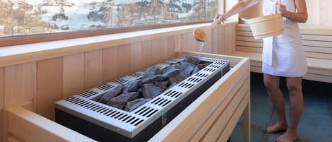 A person in a white towel standing by a sauna with a view of snow-covered mountains.