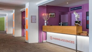 Ein Empfangstresen mit einem Schild für das Hotel 'Pierre & Vacances', einer violetten Wand und einer Holztresen.