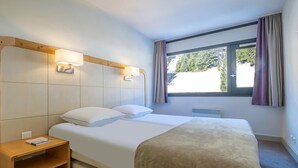 Ein Hotelzimmer mit einem Bett, Nachttischen, einem Fenster mit Vorhängen und Blick auf Grün.