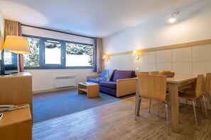 A modern hotel room with a sofa, dining table, chairs, a lamp, and a large window. - 1 BR Apartment in Flaine (Flaine)