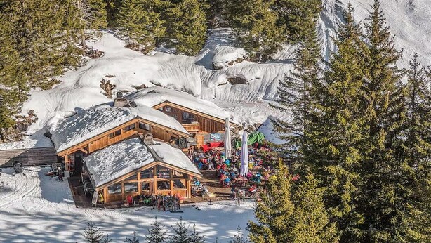 Eine Holzhütte mit schneebedecktem Dach, umgeben von Bäumen und Schnee.