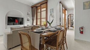 A modern living room with a sofa, dining table, and chairs, a flat-screen TV, and a fire extinguisher on the wall. - Calyra Villa by Kozystay - Ungasan (Ungasan)