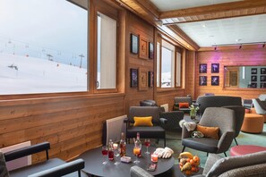 Ein gemütlicher Lounge-Bereich mit Holzwänden, großen Fenstern und Blick auf eine Skipiste.