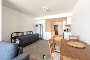 A compact living space with a sofa, a dining table with chairs, a kitchenette, and a staircase leading to an upper level.
