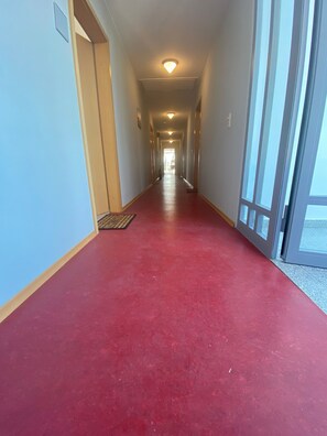 Een lange, smalle gang met een rood tapijt, lichte muren en een plafondlamp.