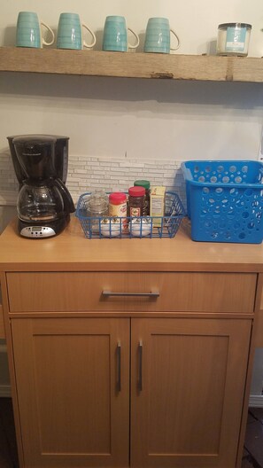 A kitchen counter with a coffee maker, a basket of items, and a blue basket. - Adorable Tiny House Near Mercedes Benz Stadium (Atlanta)