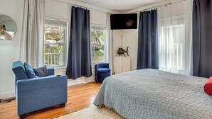 Een slaapkamer met een bed, een blauwe bank, een wit vloerkleed, een televisie aan de muur en een raam met gordijnen.