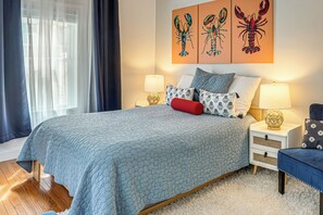 Une chambre à coucher comprenant un lit, deux tables de chevet, une commode, une fenêtre avec des rideaux et des œuvres d’art murales.