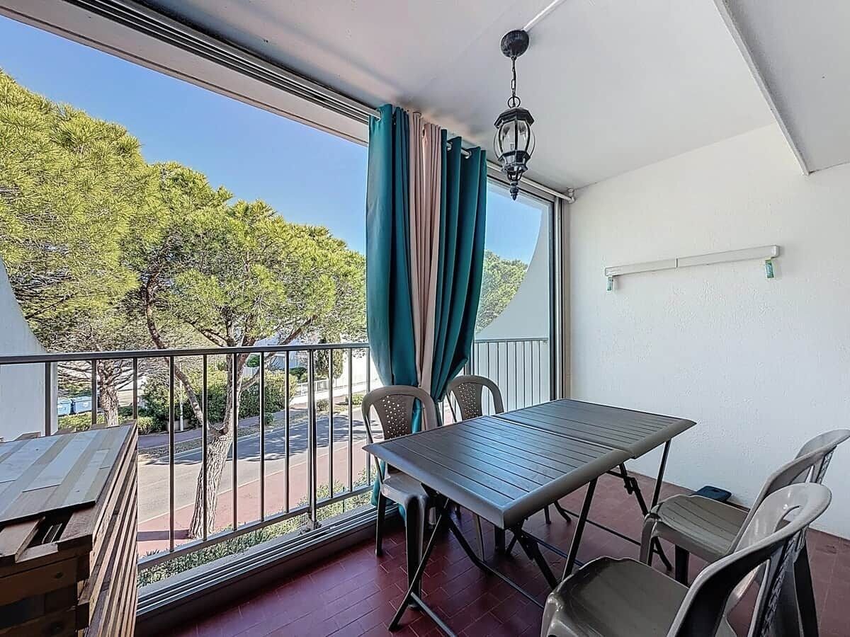 Een balkon met een tafel en stoelen, uitzicht op bomen en een weg, en een hangende lamp.