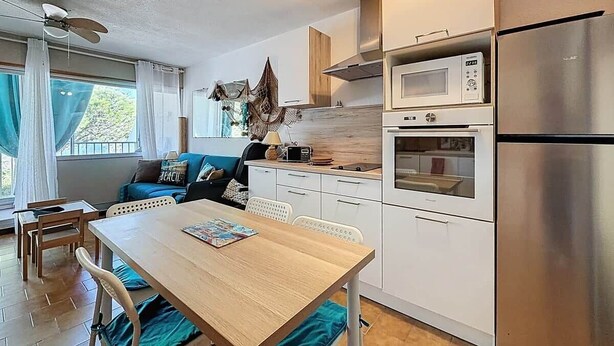 Een compacte keuken met een eettafel, witte kastjes, een magnetron, oven en een koelkast.