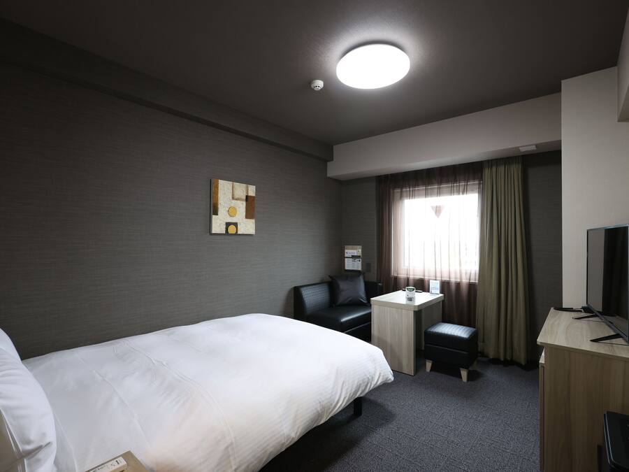A hotel room with a bed, a desk, a chair, a television, and a window with curtains.