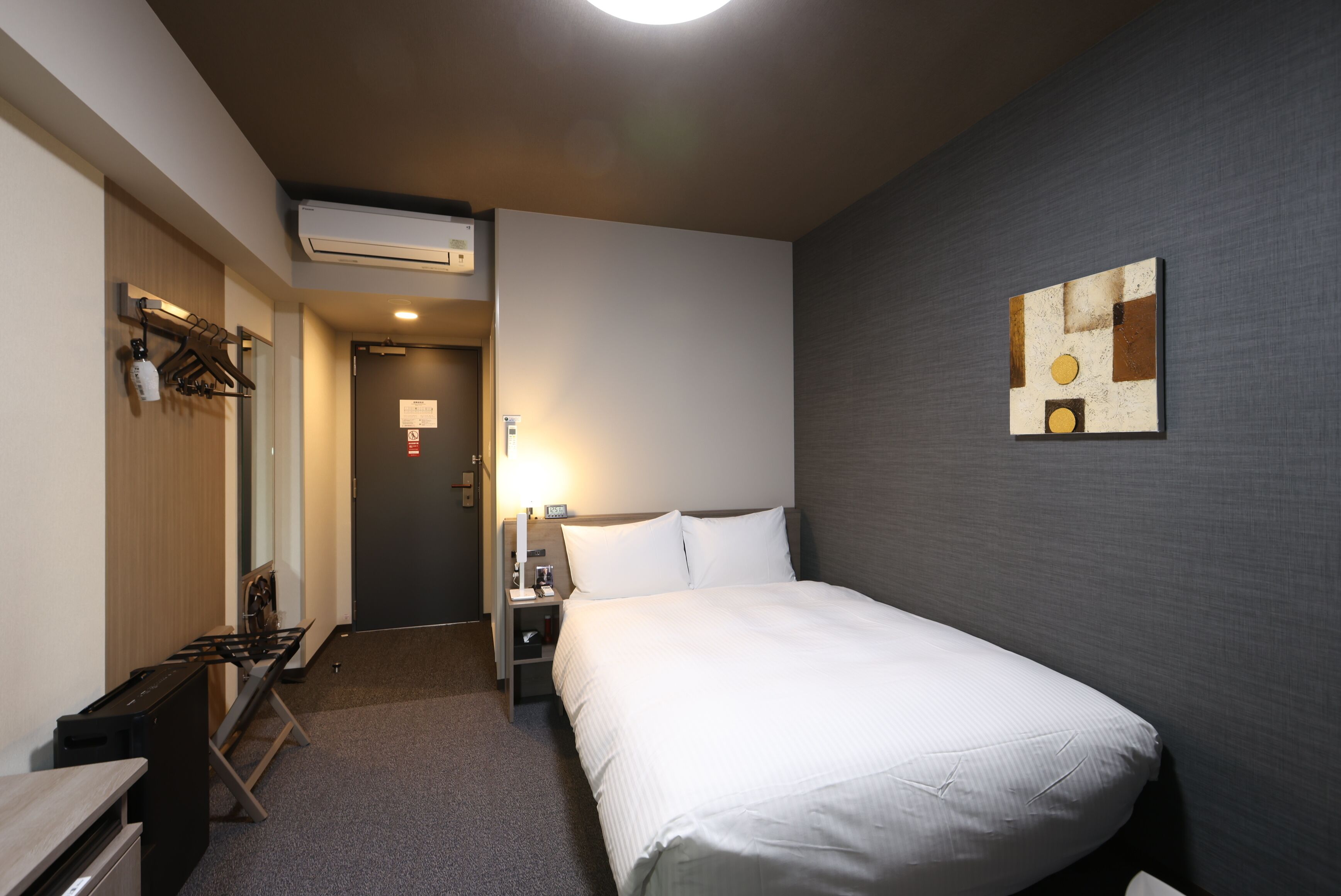 Een hotelkamer met een bed, nachtkastje, lamp en een aan de muur hangend kunstwerk.
