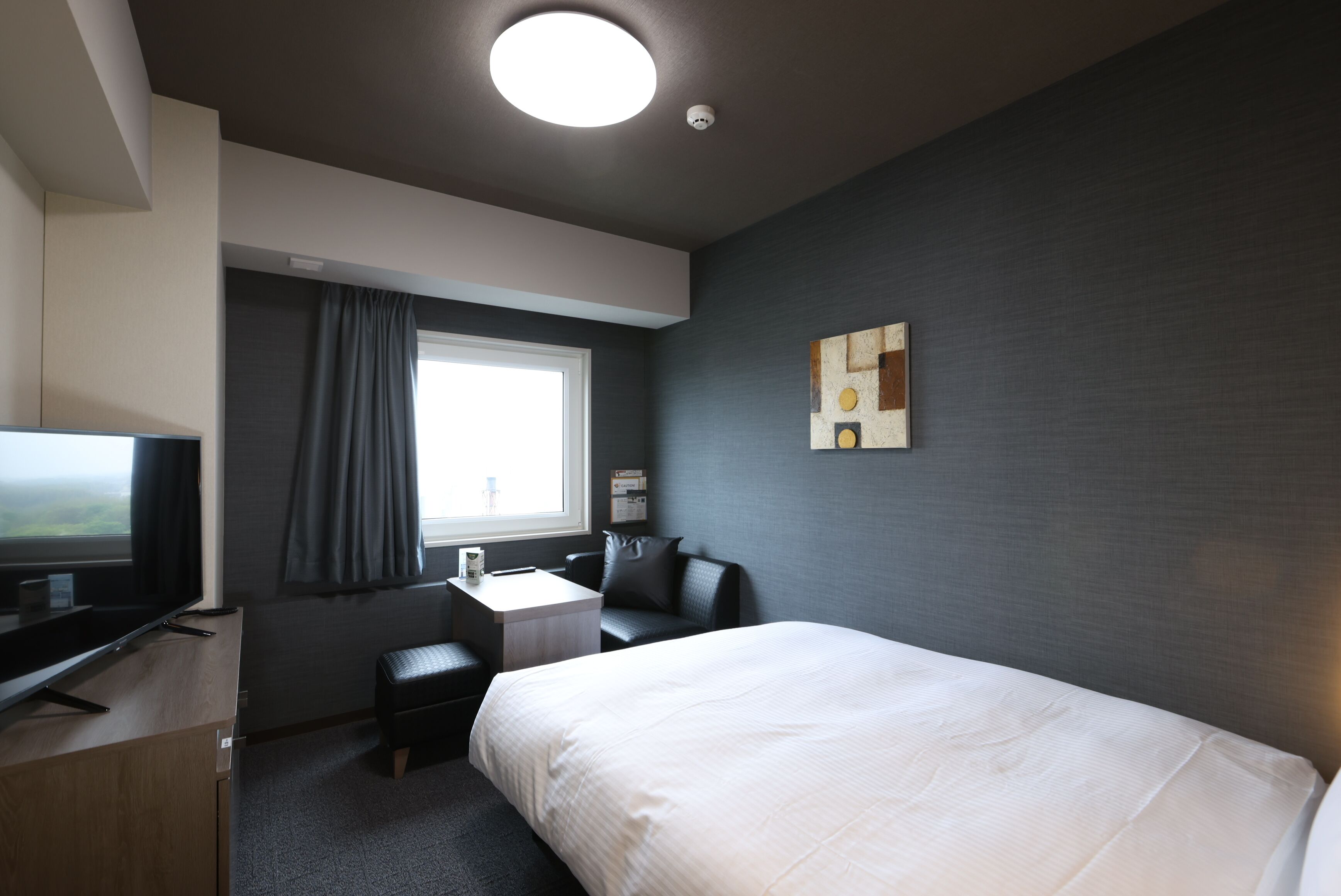 Une chambre d’hôtel équipée d’un lit, d’un bureau, d’une chaise, d’une télévision et d’une fenêtre avec des rideaux.
