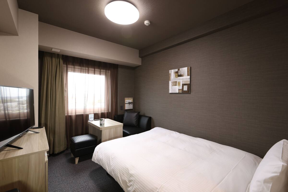 A hotel room with a bed, a desk, a chair, a television, and a window with curtains.