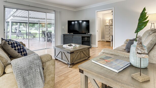 A living room with a TV, a coffee table, a sofa, and a dining area with outdoor seating. - Golf Course Getaway! Port St Lucie Home w/ Lanai (Port St. Lucie)
