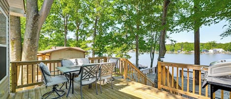 A wooden deck with outdoor furniture, a grill, and a view of a lake.