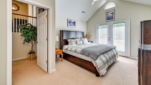 Ein Schlafzimmer mit einem Bett, einem Deckenventilator, einer Zimmerpflanze und einer Tür, die zu einer Treppe führt.